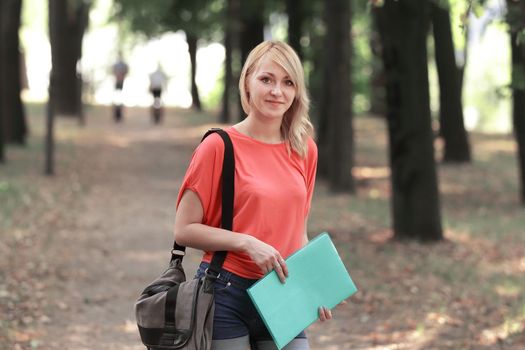 successful female student with a bag and a clipboard on the background of the Park