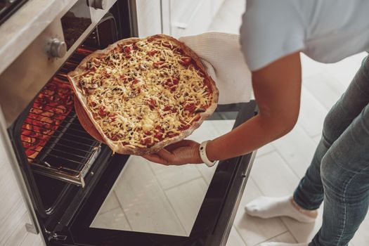 A woman puts pizza on the baking tray in the open oven