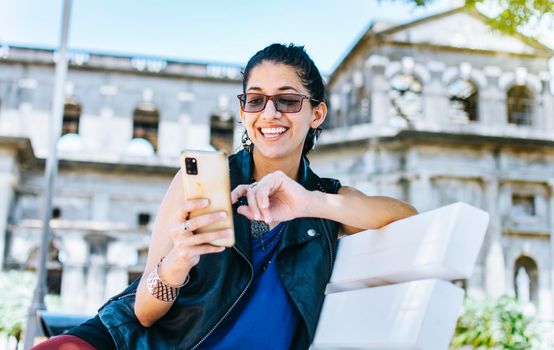 An attractive girl sitting on the cell phone smiling, Girl sitting on a bench texting on her cell phone, Urban style girl sitting on a bench with her cell phone
