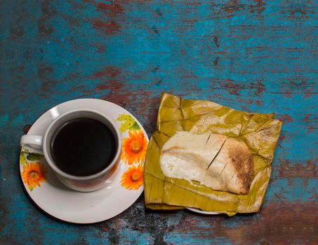 Stuffed tamale served on wooden table, stuffed tamale on banana leaf served with a cup of coffee on wooden table, typical nicaragua food