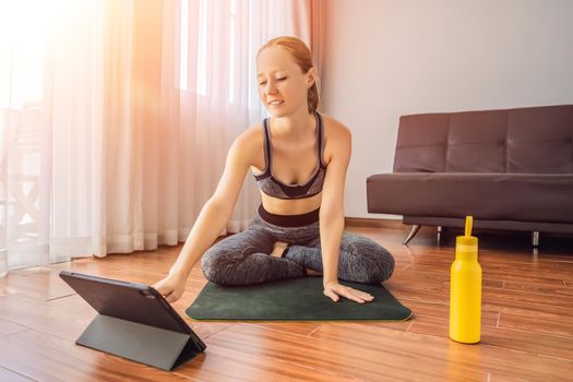 Fitness woman exercising on the floor at home and watching fitness videos in a tablet. People do sports online because of the coronovirus