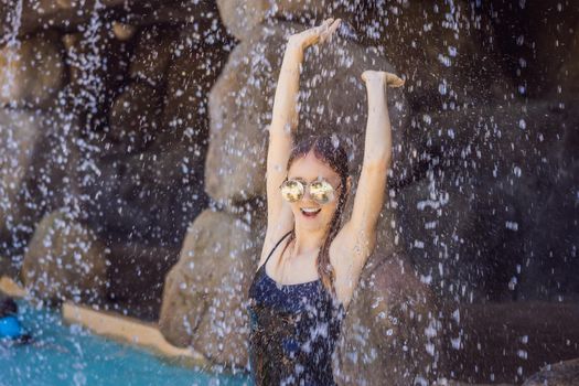Young joyful woman under the water stream, pool, day spa, hot springs
