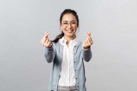 Emotions, people and lifestyle concept. Optimistic good-looking asian female in glasses, showing korean hearts gesture with fingers and smiling, express love sympathy and admiration