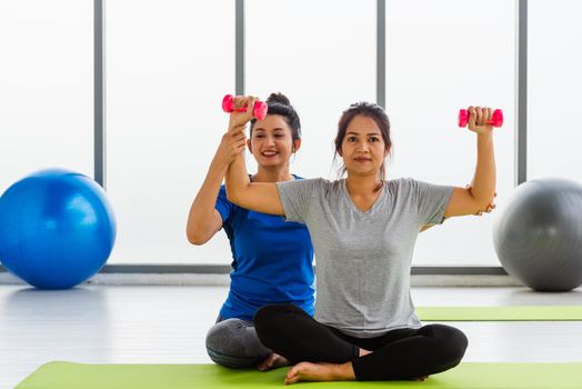 woman teacher teach adult student doing yoga hands holding dumbbells