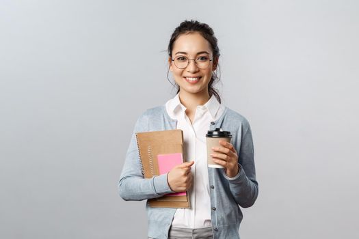 Education, teachers, university and schools concept. Attractive young smiling woman working, teaching students with online app, carry books and notebooks, drinking coffee on her way to class