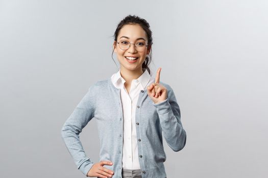 Education, studying and online classes concept. Rule number one. Cheerful pretty asian girl explaining exercise to class, raising index finger, pointing up, add a suggestion or making point, smile