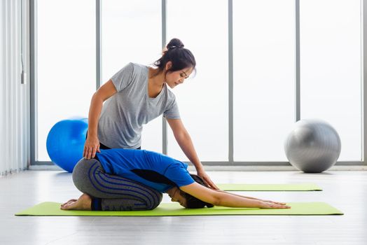 woman teacher teach adult student doing yoga stretching position in studio