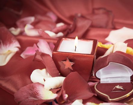 candle and a diamond ring on a background of rose petals