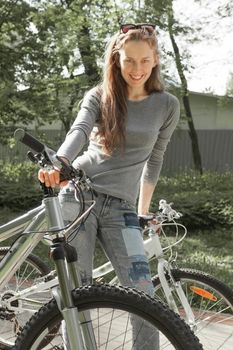 smiling young woman with bike standing in city Park.