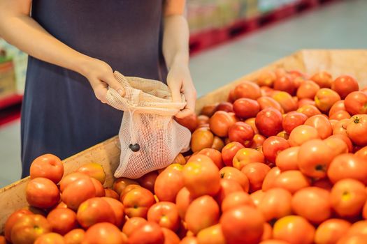 A woman chooses tomatoes in a supermarket without using a plastic bag. Reusable bag for buying vegetables. Zero waste concept