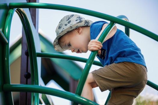 Little boy very focused climb on the green tube ladders in playground.