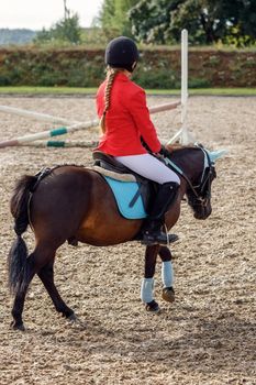 Girl in red riding clothing riding on pony over small jumps