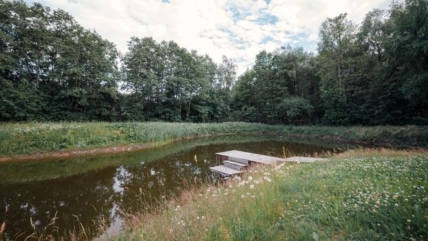 Pond in the village next to the forest with a wooden bridge with steps for fishing and relaxation.