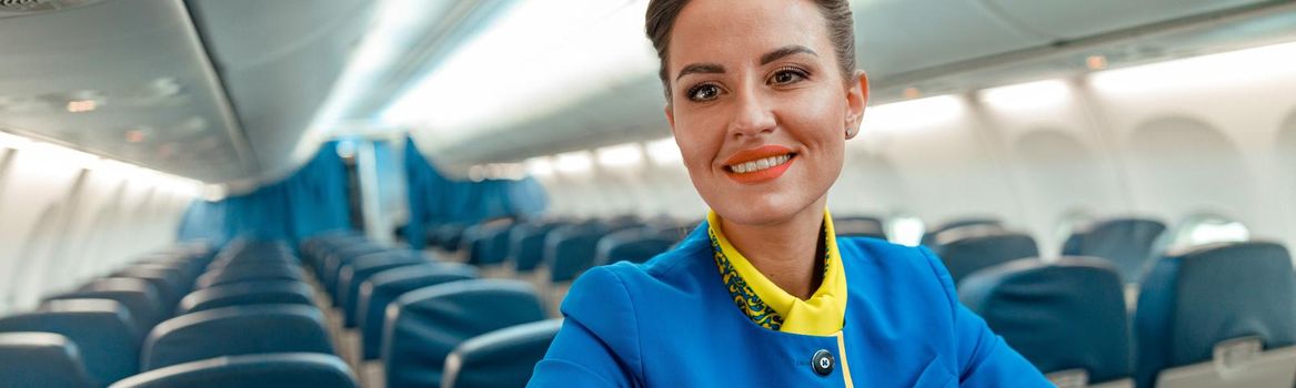 Cheerful woman stewardess standing in airplane passenger salon