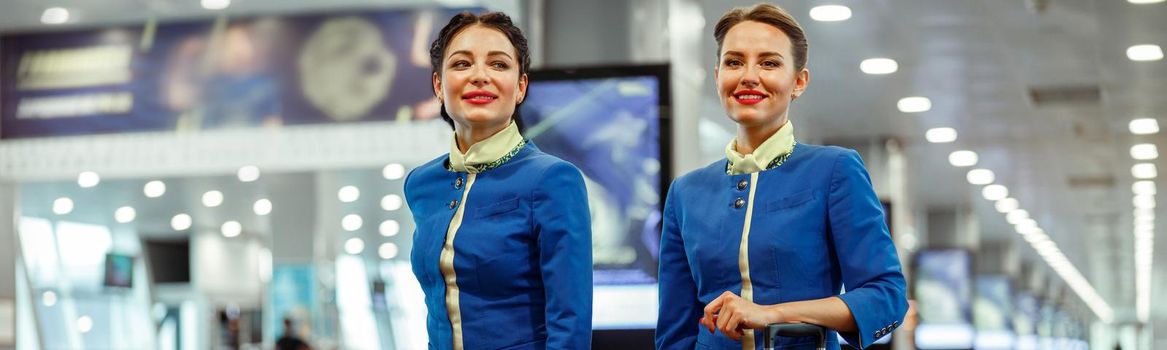 Joyful women stewardesses walking down airport terminal