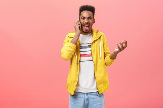 Guy fighting having rough argument with girlfriend via phone call yelling in smartphone gesturing from anger and rage holding device near ear shouting pissed over pink background
