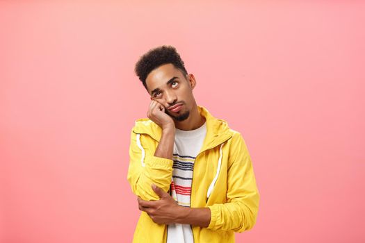 Waist-up shot of bored irritated african american man with beard and afro haircut leaning head on palm in indifferent and careless pose being tired of annoying boring talks over pink background