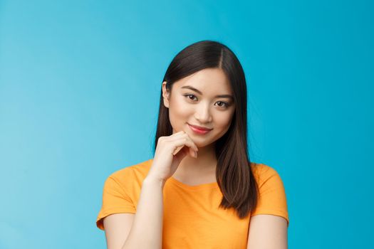 Close-up coquettish good-looking asian young modern woman curiously listen interesting story, smirking relaxed gaze camera, touch chin thoughtful, intrigued stand blue background
