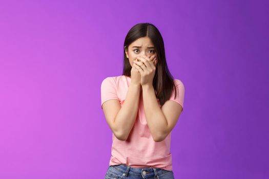 Shocked female asian victim frightened, gasping witness crime, close mouth hands, frowning, stare camera scared upset, make innocent terrified gaze, stand purple background