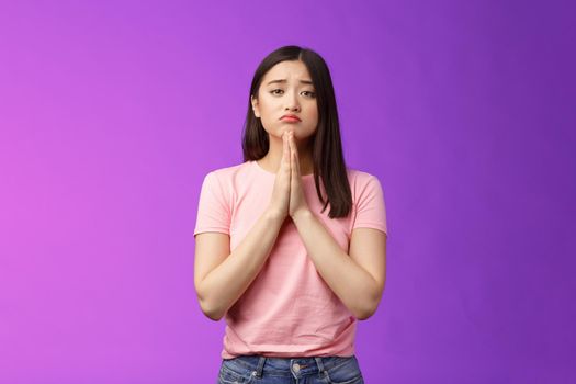 Gloomy cute asian daughter begging mother buy new phone, supplicating, hold hands pray, sulking frowning pretty please, asking apology, pleading favor, stand purple background
