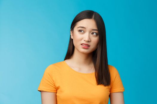 Doubtful unsure cute asian girl dark short haircut look left questioned, see strange thing, open mouth frowning upset uncertain, have hesitations, peek suspicious aside, stand blue background