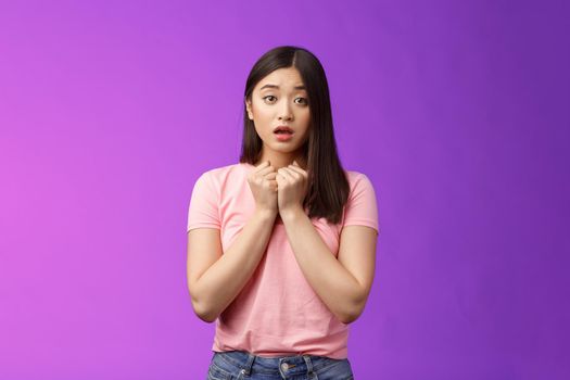 Timid concerned cute asian girl express empathy and worry, press hands heart upset, sorry for friend, open mouth, sighing sad nervous, hesitating, anxiously saying love you, stand purple background