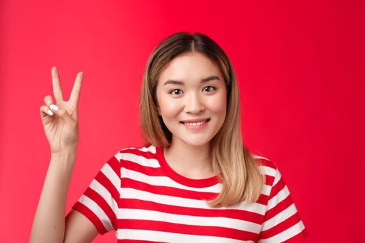 Close-up cheerful glad young attractive blond woman wear striped t-shirt smiling friendly make order, reservation for two show victory peace sign, stand red background, wanna be second