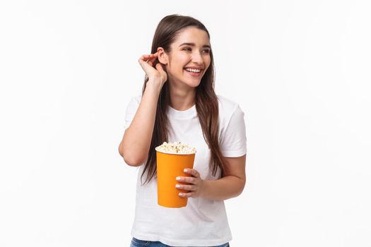 Entertainment, fun and holidays concept. Portrait of beautiful young carefree friendly woman in glasses, place hair strand behind ear giggle joyful watching movie in cinema, eating popcorn