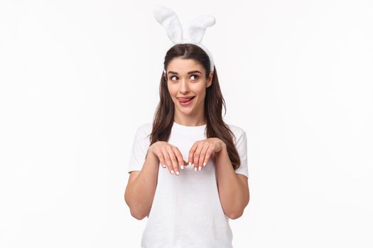 Funny and silly, playful girl in rabbit ears, t-shirt, looking away and licking lips, daydreaming about something delicious on Easter day, imitating bunny with hands pulled close to chest like paws