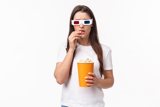 Entertainment, fun and holidays concept. Waist-up portrait of serious-looking focused young woman watching intense scene in movie, frowning and eating popcorn, look 3d film with interest
