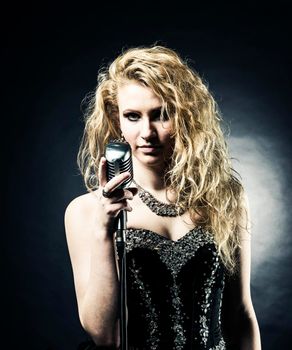 beautiful blonde woman singer in a black dress holding a microphone and sings a song.