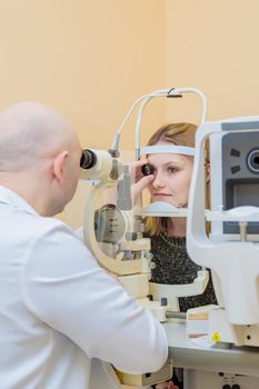 A male ophthalmologist checks the eyesight of a young girl using a modern device with a light beam