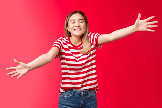 Silly friendly-looking tender blond asian girl close eyes smiling broadly toothy upbeat smile extend arms, wanna give tight hug, reach camera move forward cuddle best friend, red background