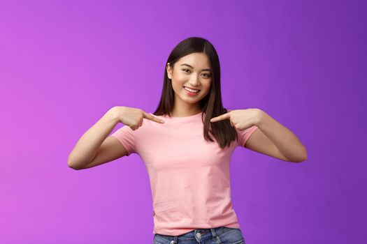 Active energized friendly tender asian stylish girl introduce herself, pointing chest proudly, smiling boastful, describe own achievements, bragging accomplishments, stand pleased purple background