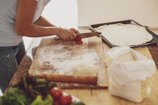 The process of cooking pizza at home with rolled dough on a baking tray and cutting vegetables