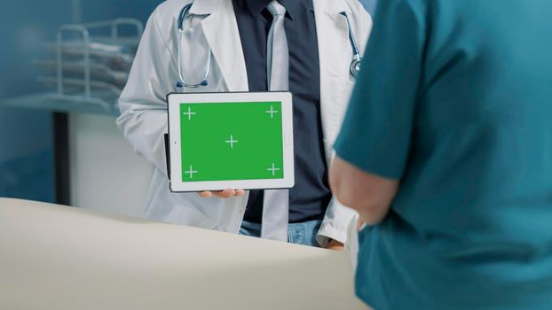 Male doctor holding horizontal green screen on digital tablet