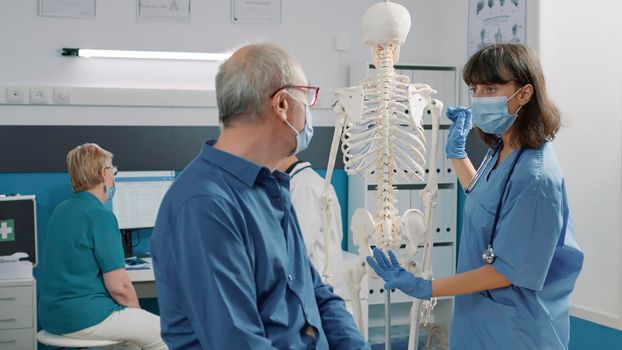 Nurse with face mask explaining bones on human skeleton