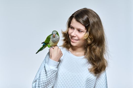 Child girl with pet green quaker parrot looking at camera on light studio background