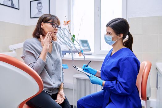 Dental office visit, female patient talking to doctor, dentist making notes