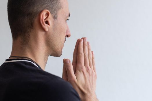 Man praying. Concentrated young man in white shirt holding hands clasped near face while standing against grey background