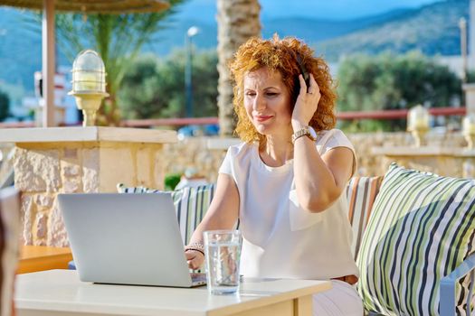 Middle age business woman in headphones using laptop outdoor