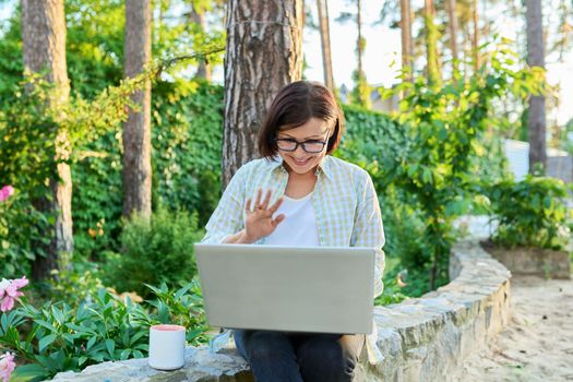 Middle age woman with laptop cup resting working in the backyard.