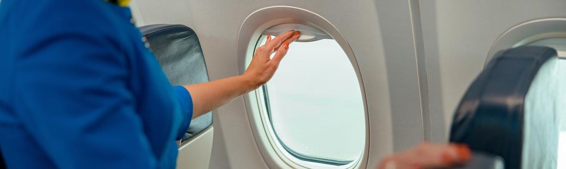 Female flight attendant closing window in airplane