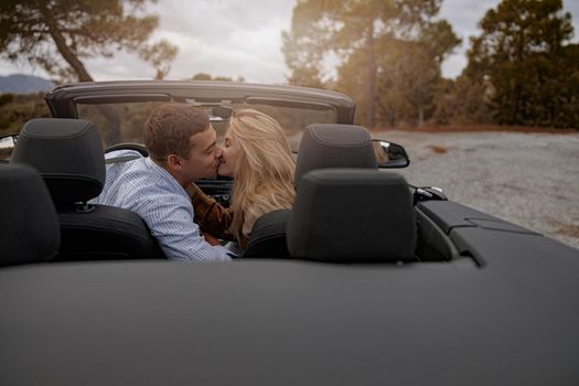 Happy man and beautiful woman sitting in convertible car outdoor and kissing, love concept