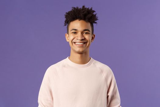 Close-up portrait of cheerful young hipster guy with dreads, smiling optimistic and delighted, standing purple background, having lucky good day, express positivity and joy