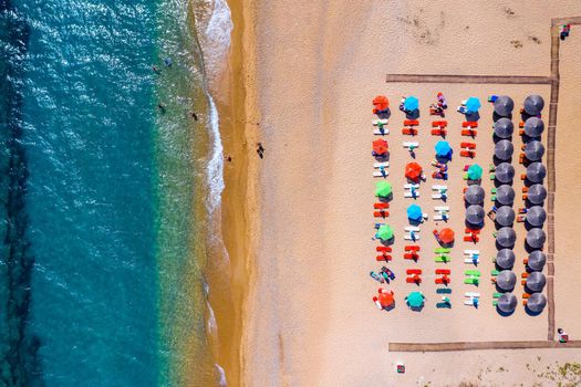 View from above, stunning aerial view of an amazing beach with beach umbrellas and turquoise clear water. Top view on sun loungers under umbrellas on the sandy beach. Concept of summer vacation. 