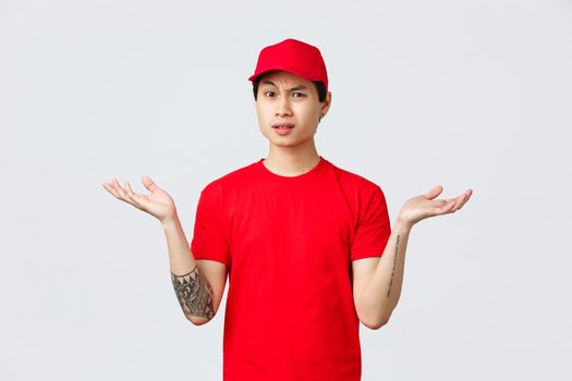 Express delivery, shipping and logistics concept. Courier dont understand why, wearing red cap and t-shirt, shrugging with hands spread sideways, grimacing bothered, complain