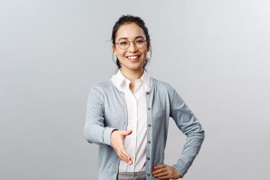 Lifestyle, people and emotions concept. Nice to meet you. Portrait of enthusiastic smart young woman in glasses, greet business partner, extend hand for handshake during meeting, grey background