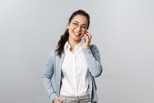 Office lifestyle, business and people concept. Friendly asian female in glasses, white collar shirt, laughing and looking away casually talking on phone, have conversation use mobile connection