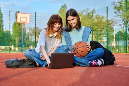Friends students sitting on school basketball court looking at laptop